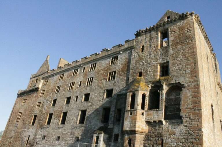 The ruined south facade of Linlithgow Palace, oriel windows and battlements against a clear sky